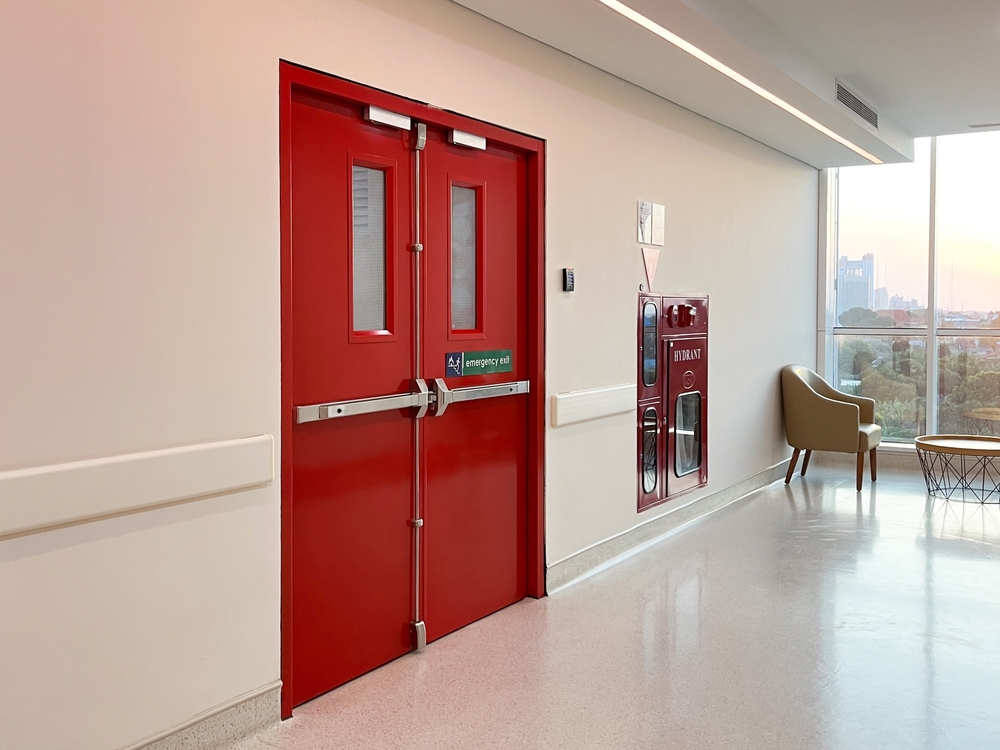 Red double fire doors with push bars in a hospital corridor