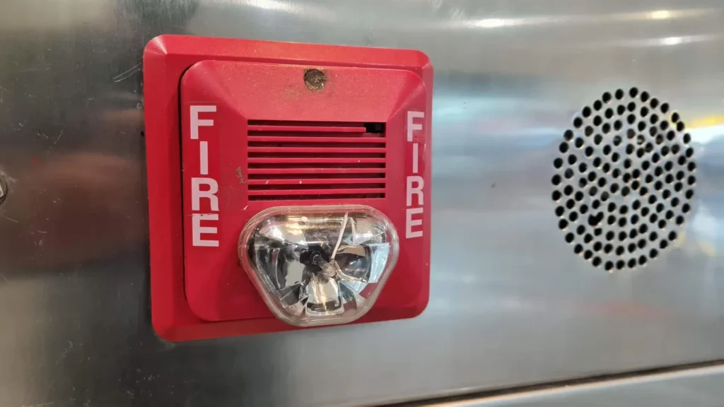 Red fire alarm horn and strobe mounted on a metal panel